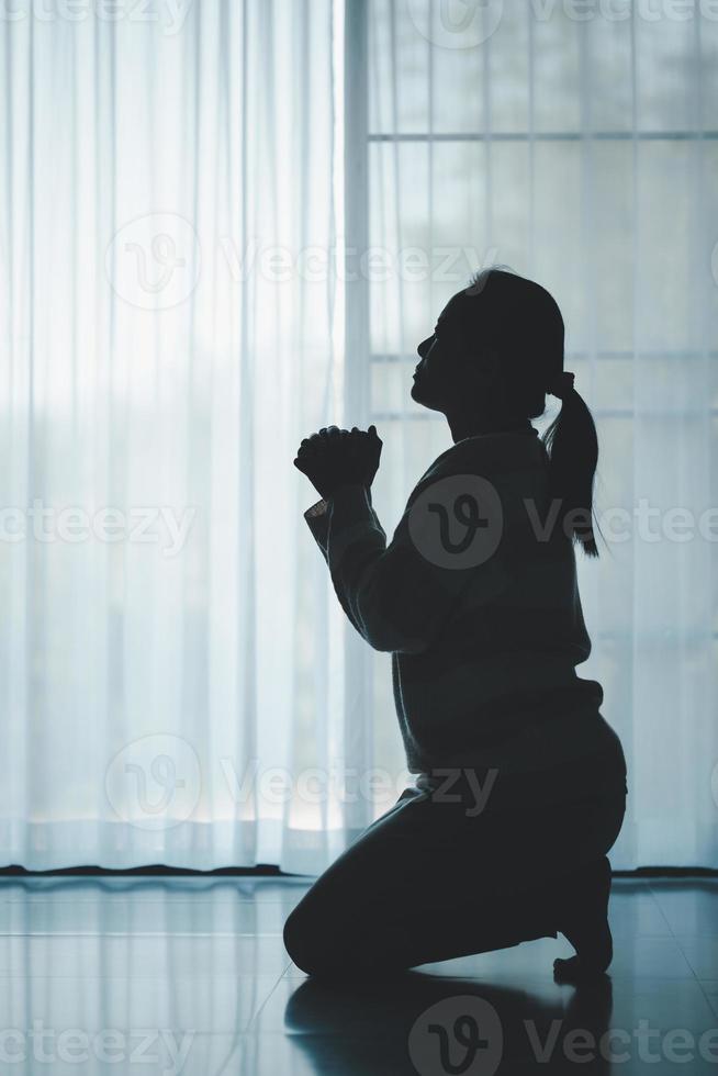 silueta de mujer arrodillado y Orando en moderno Iglesia a puesta de sol tiempo. hembra católico oración Adoración a Dios deseo un mejor vida en hogar a amanecer con creer fe. concepto de adoradores arrodillado foto