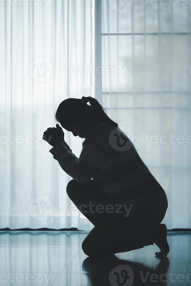 silhouette of woman kneeling and praying in modern church at sunset time. Female catholic prayer worship to God wish a better life in home at dawn with believe faith. concept of worshipers kneeling. photo