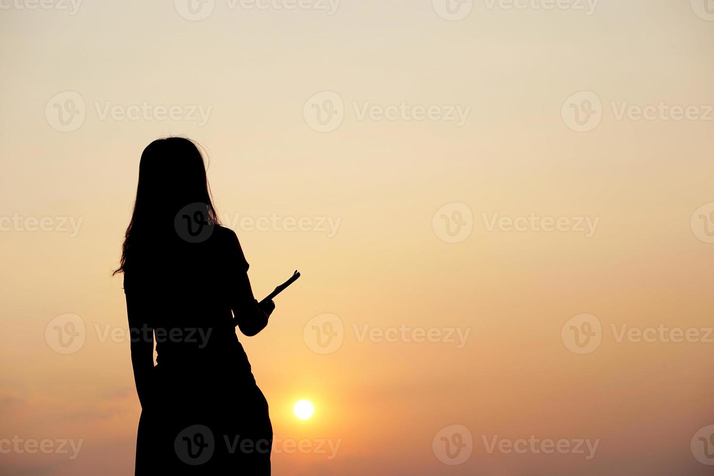 silhouette of a woman holding a computer sunset background photo