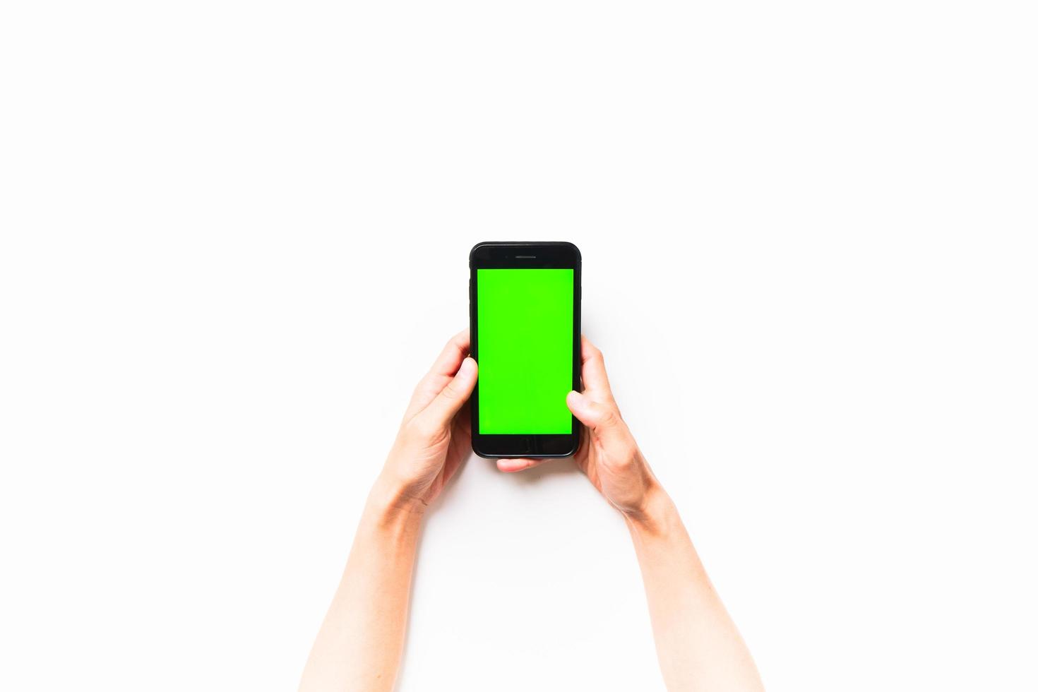 Woman hand holds mobile smartphone with green screen in vertical position isolated on green background with thumbs up finger. Mock up mobile screen blank space photo