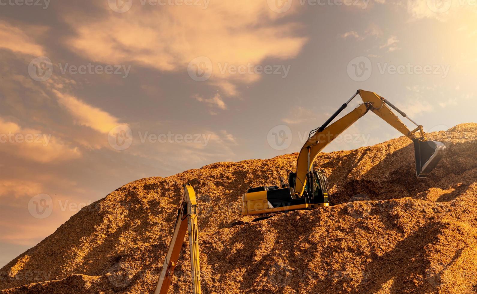 Backhoe working on huge sawdust pile in paper production factory. Bucket of digger digging wood chips. Pile of wood chips from pulp mill against the sky. Pulp and paper industry. Bulldozer  working. photo