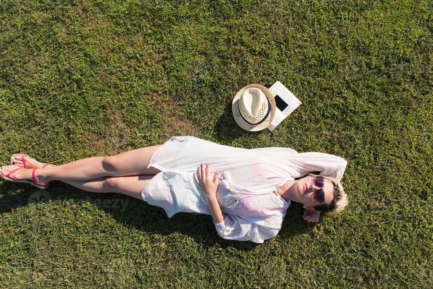 Top view from above of a woman lying and relaxing on a meadow covered with green grass on a sunny summer or spring day. photo