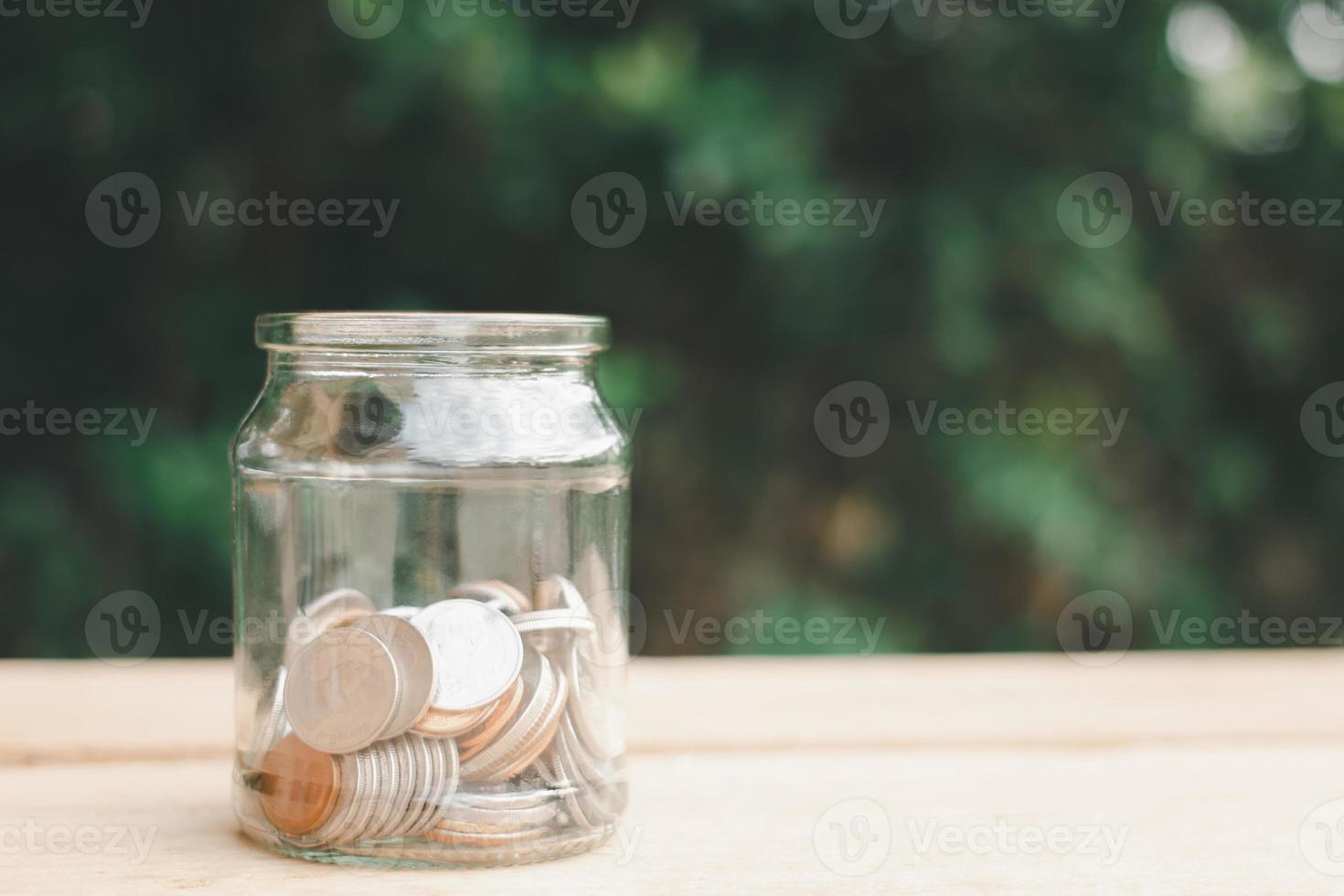 Coins in half clear jar placed on wooden planks outdoors in the garden, investment saving concept.copy space. photo