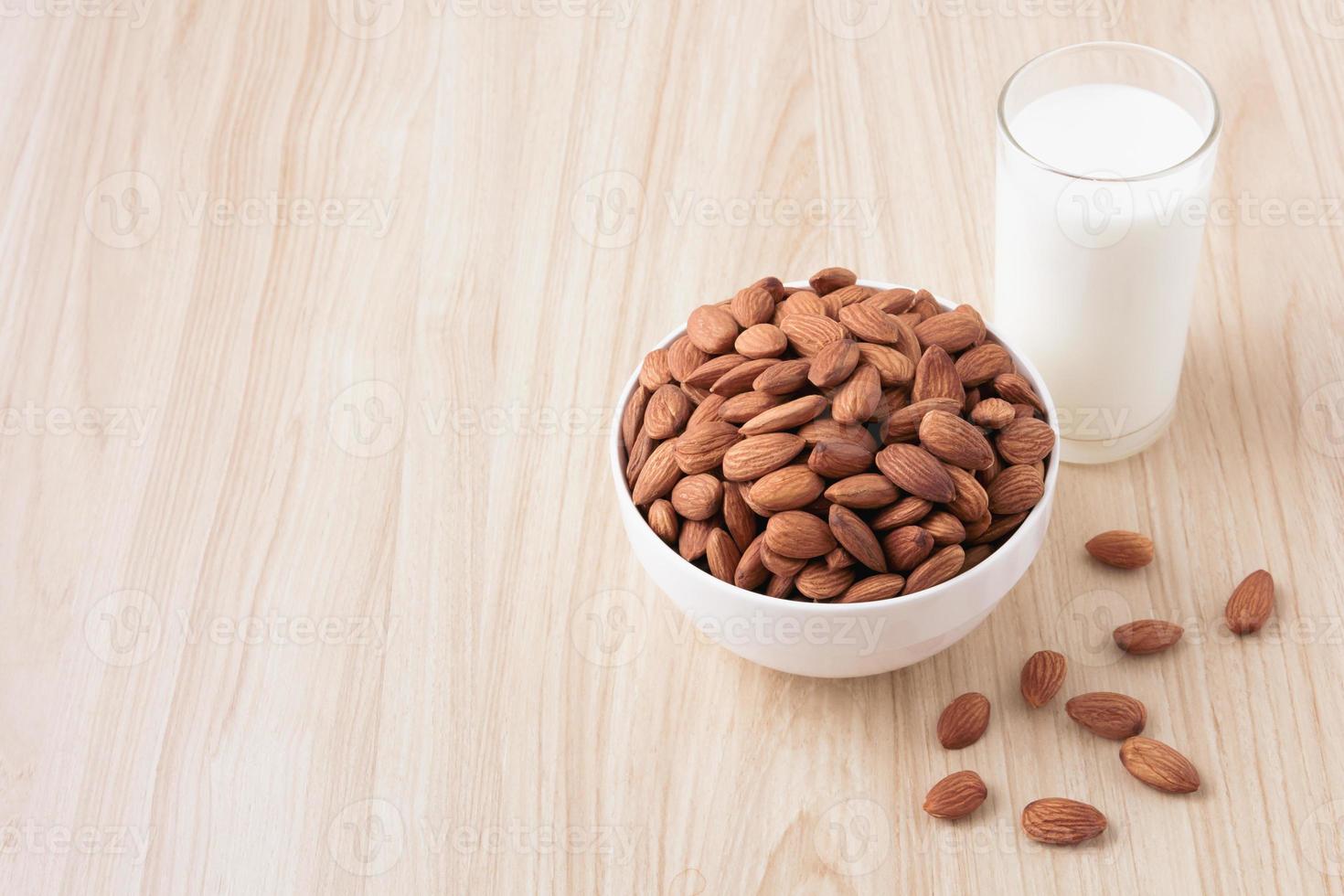 Almond nuts in a white bowl and milk in glass on wood background with nuts around the bowl.selective focus.front view.copy space. photo