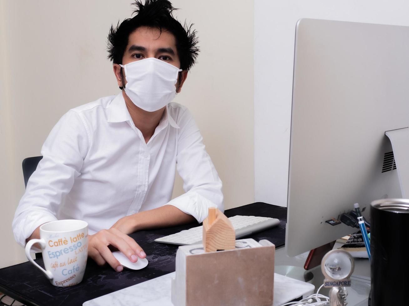 joven asiático con mascarilla trabajando en una computadora portátil durante la pandemia del coronavirus foto