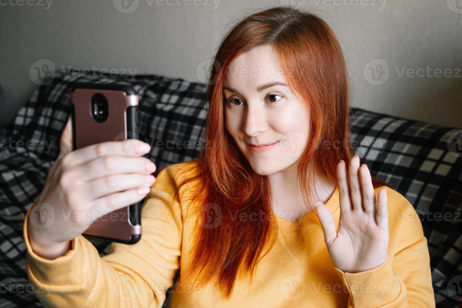 Young red-haired woman communicates online using smartphone. photo