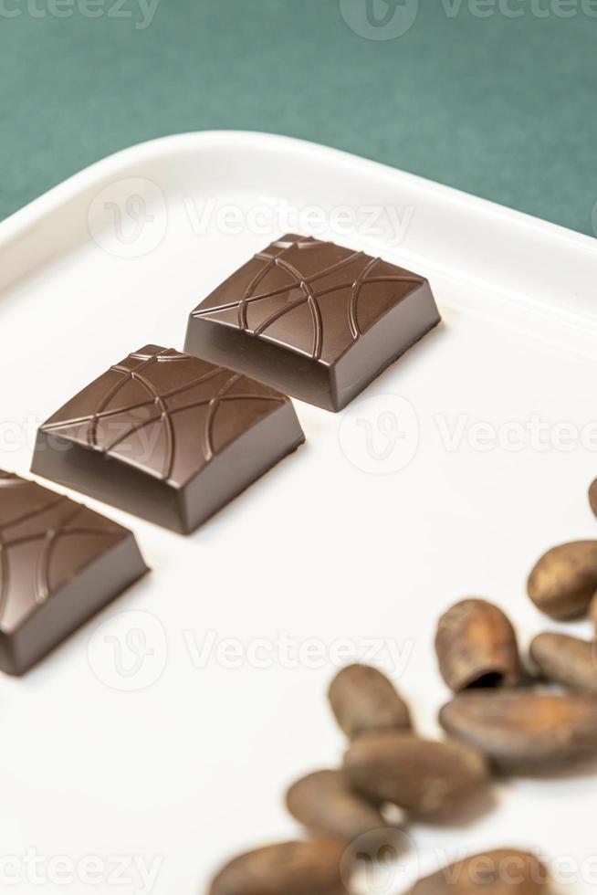 Handmade bitter chocolates on white plate with cocoa beans on green background. photo
