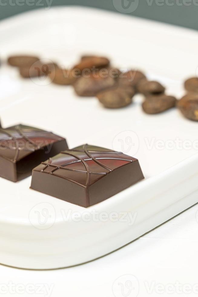 Handmade bitter chocolates on white plate with cocoa beans on green background. photo