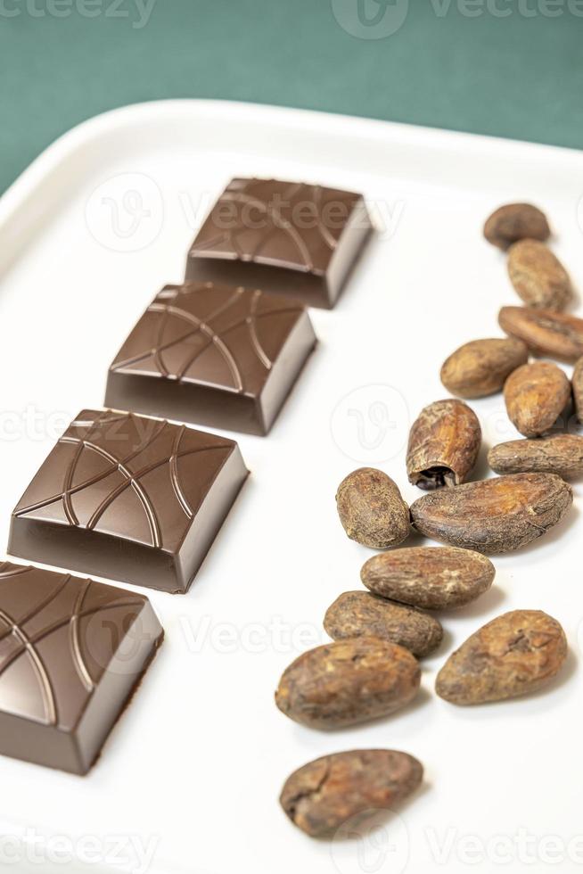 Handmade bitter chocolates on white plate with cocoa beans on green background. photo