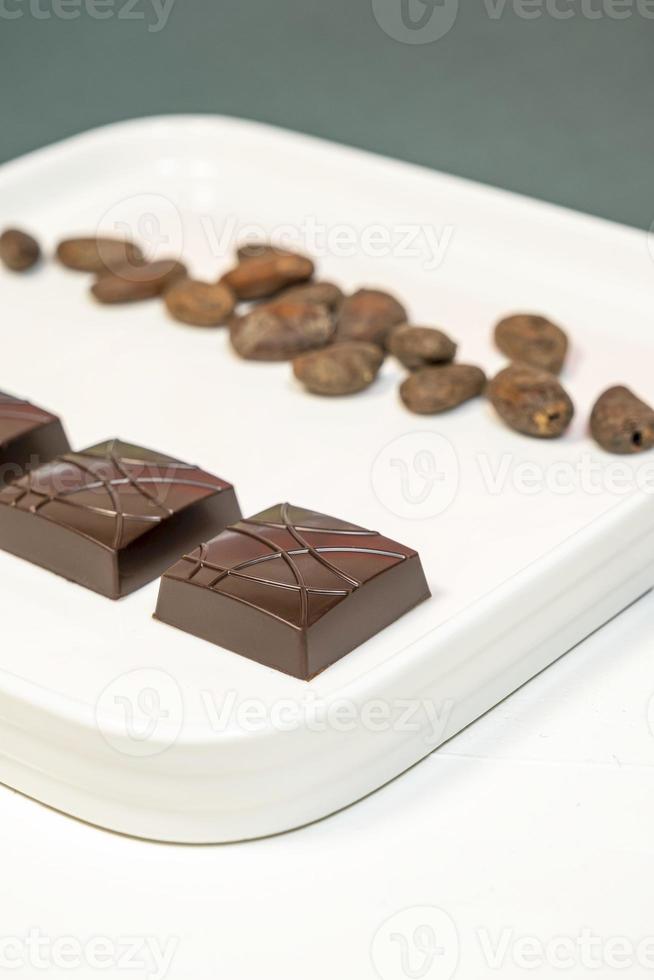 Handmade bitter chocolates on white plate with cocoa beans on green background. photo