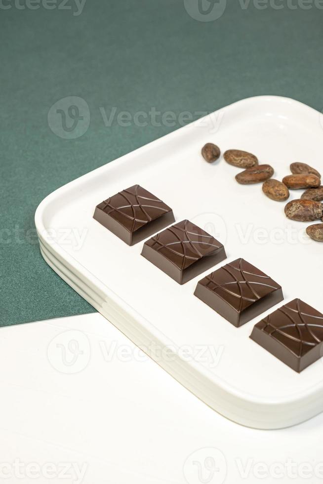Handmade bitter chocolates on white plate with cocoa beans on green background. photo