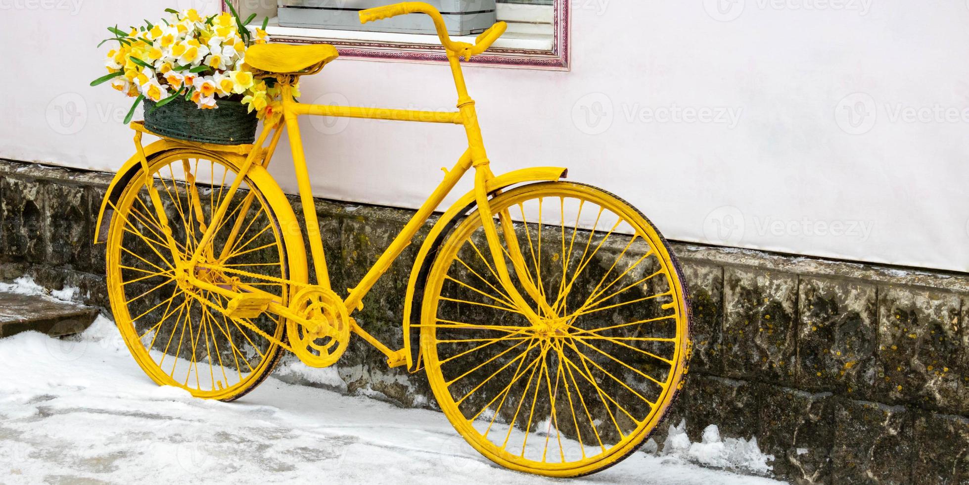 An old yellow bicycle stands against a wall in winter, in vintage style photo
