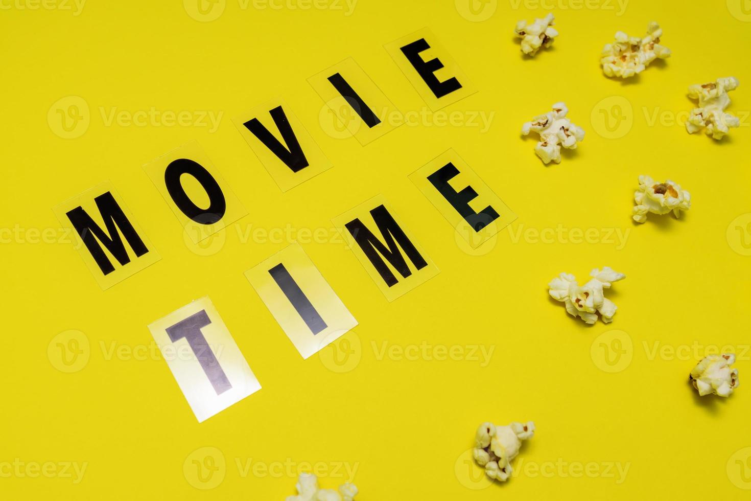 Movie Time text lettering with scattered salty popcorn on yellow background photo