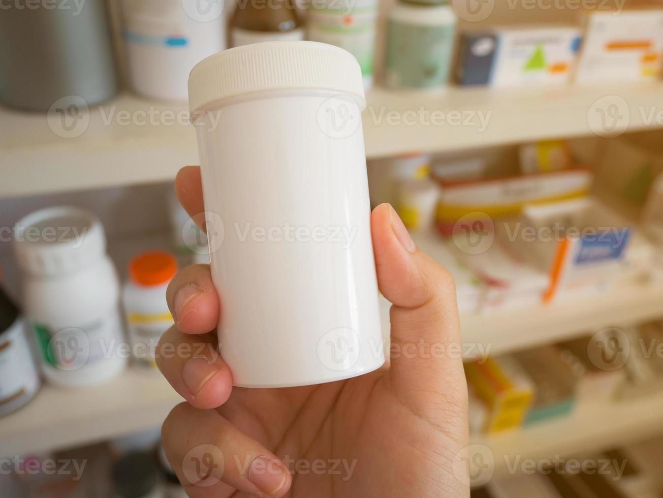 cierre la mano del farmacéutico sostenga los frascos de medicamentos en los estantes de las drogas en la farmacia foto