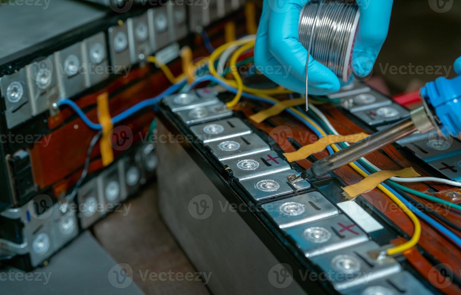 Technician use soldering iron to solder metal and wire of lithium-ion rechargeable battery. Repair module of Li-ion battery. Engineer hand holds soldering iron and tin-lead to solder electronic board. photo