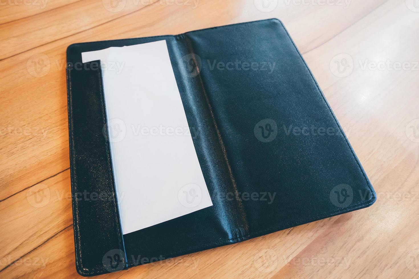Blank empty white paper in black leather restaurant payment billing receipt folder on wood table photo