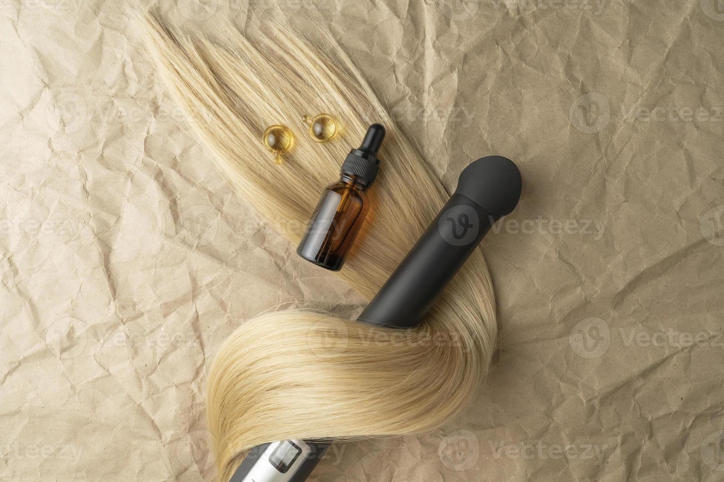 A hair treatment essential oil for smoothing hair lying on a strand of blond hair photo