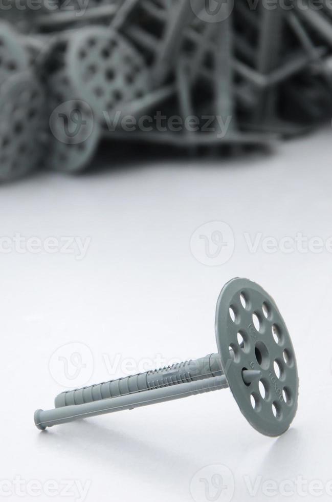 A gray plastic dowel fastening for thermal insulation with round umbrella caps lies on a gray foam polystyrene plate photo