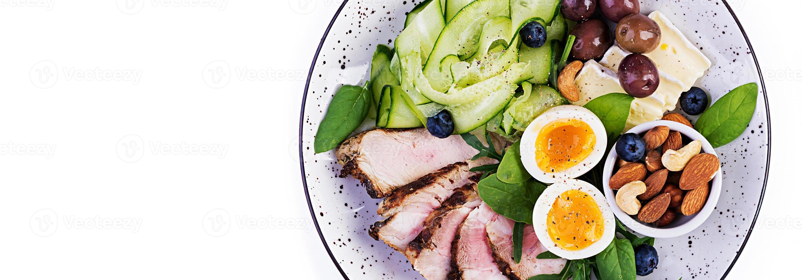 Ketogenic diet. Keto brunch. Boiled egg, pork steak and olives, cucumber, spinach, brie cheese, nuts and blueberry. Banner. Top view photo