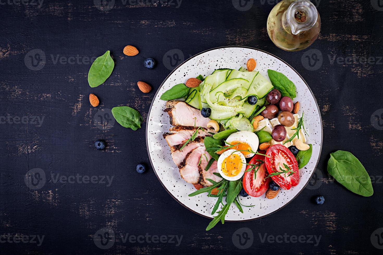 Ketogenic diet. Keto brunch. Boiled egg, pork steak and olives, cucumber, spinach, brie cheese, nuts and tomato. Top view photo
