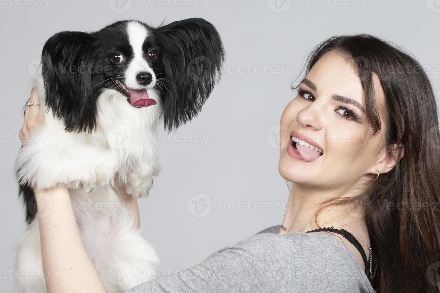 un linda joven mujer es abrazando su Papillon cachorro. amor Entre propietario y perro. niña y perro espectáculo lengua juntos. foto