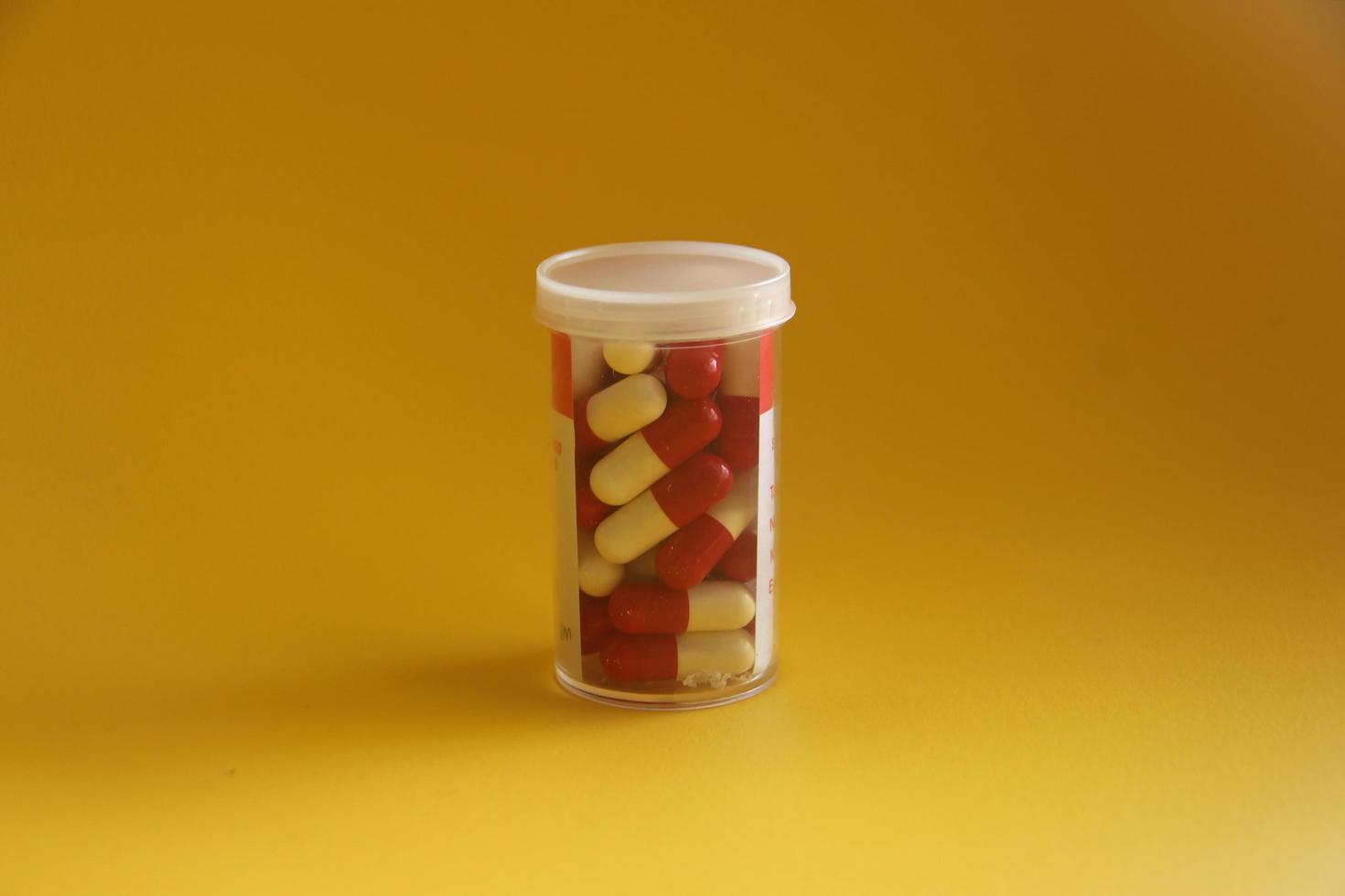 Red and white medical pills tablet capsule inside small clear container with paper lables isolated on yellow background. photo