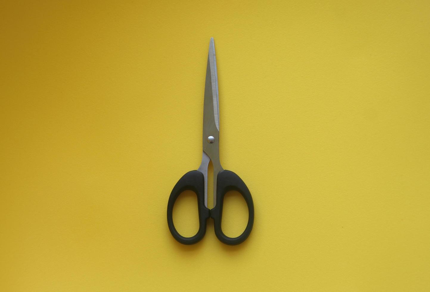 Black stainless steel scissors isolated photo on yellow background. School or office tools equipment object.