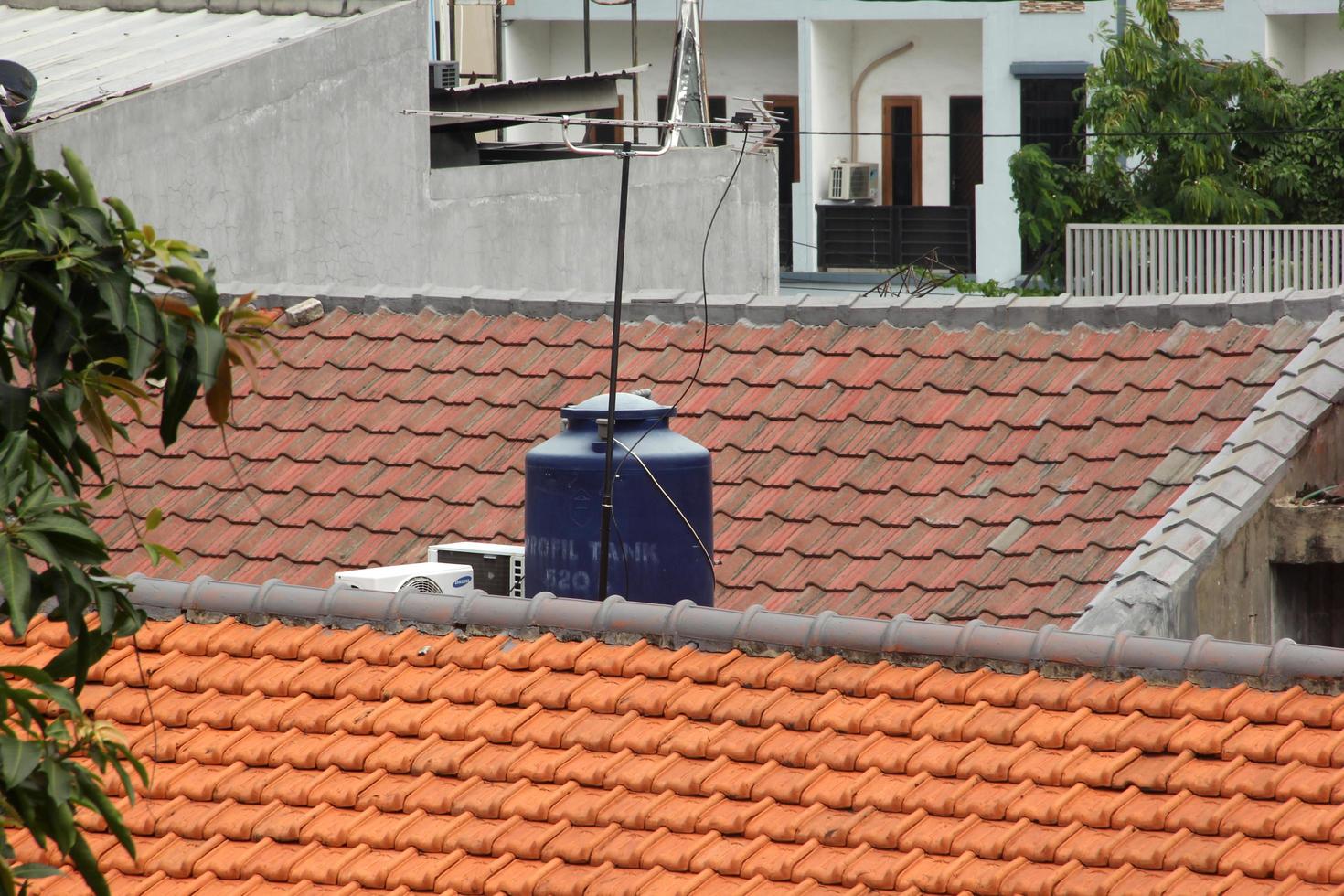 West Jakarta, Indonesia - February 10th, 2023 -  Blue Water tank on house roof top with buildings background isolated on rectangle template. photo