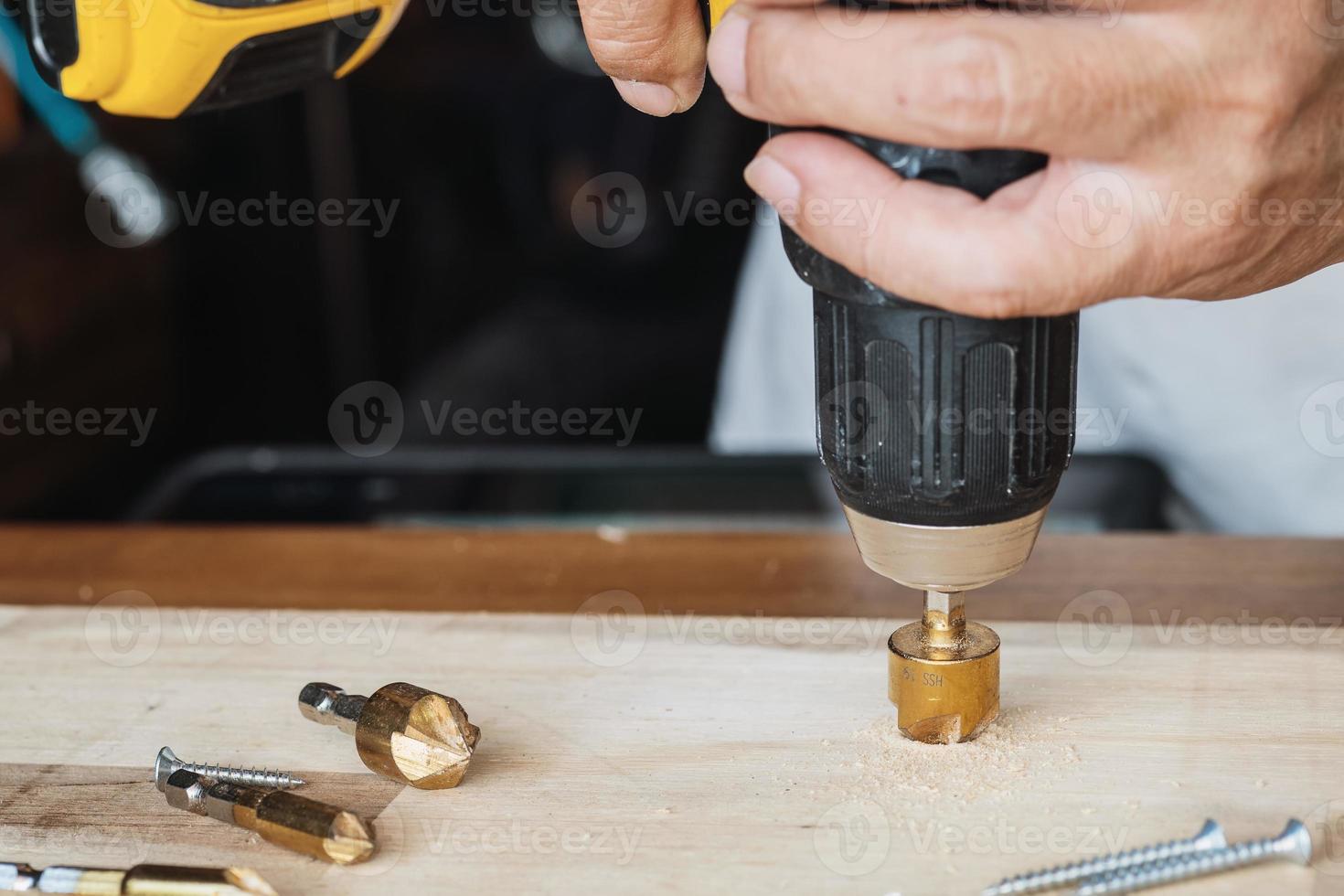 carpintero utilizar avellanar poco a perforar ambos un piloto agujero y utilizar avellanar poco a receso el cabeza de el tornillo dentro madera tablón. bricolaje fabricante y carpintería concepto. selectivo atención foto