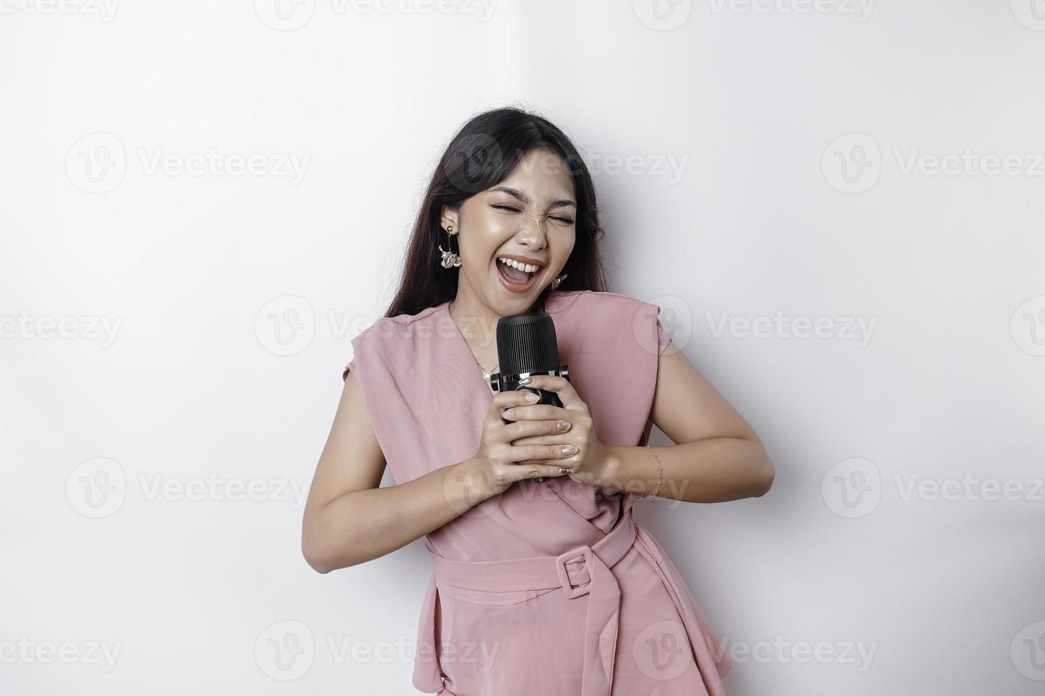 Portrait of carefree Asian woman, having fun karaoke, singing in microphone while standing over white background photo