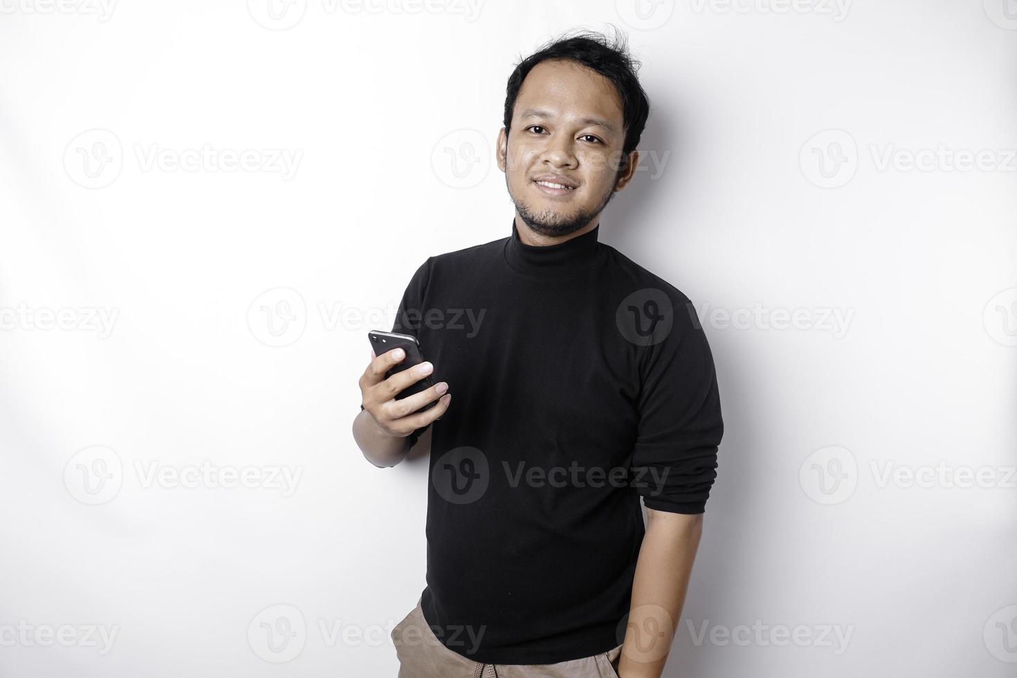 Excited Asian man wearing black shirt smiling while holding his phone, isolated by white background photo