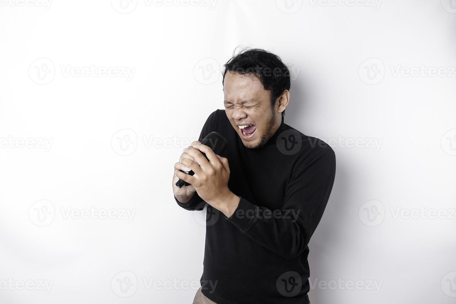 Portrait of carefree Asian man, having fun karaoke, singing in microphone while standing over white background photo