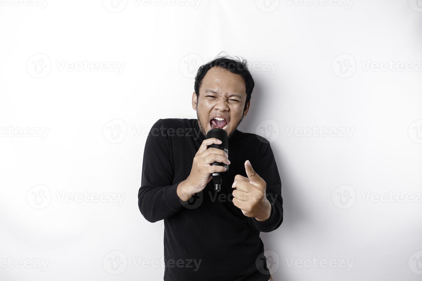 Portrait of carefree Asian man, having fun karaoke, singing in microphone while standing over white background photo