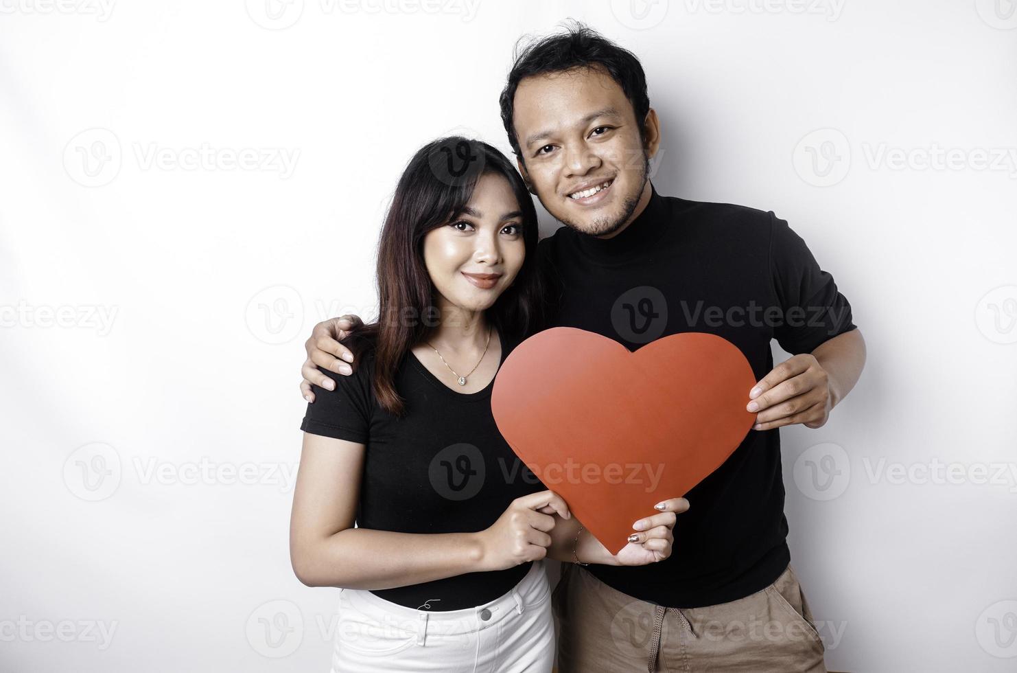 A young Asian couple smiling and holding red heart-shaped paper, isolated by white background photo