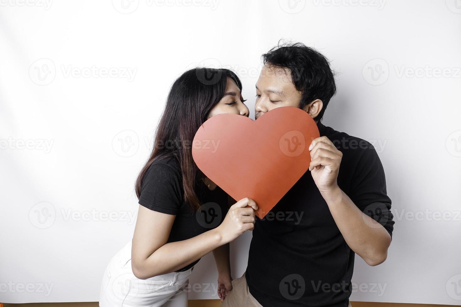 un Pareja en amor sostiene un papel rojo corazón, cubierta su caras. contento San Valentín día foto