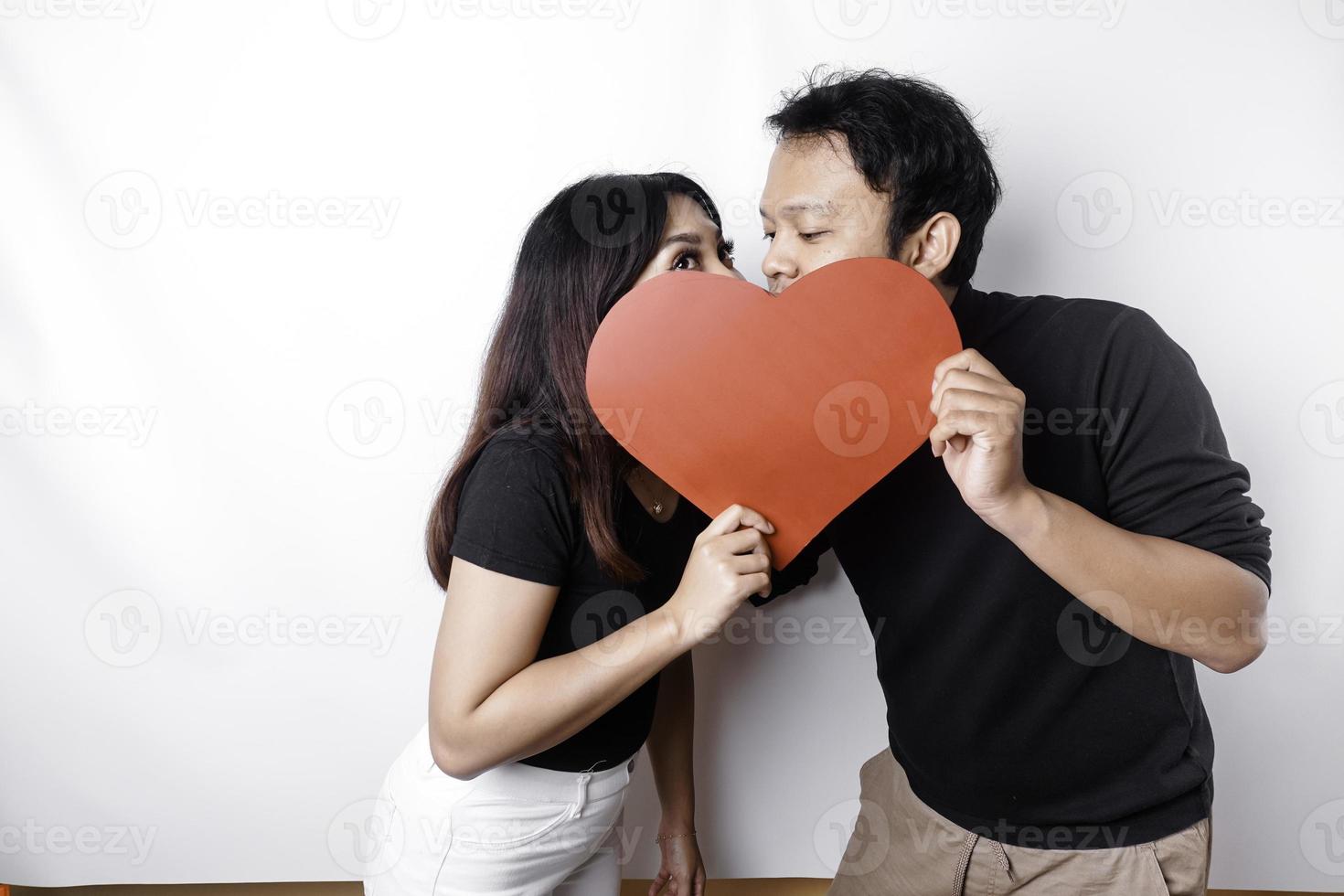 un Pareja en amor sostiene un papel rojo corazón, cubierta su caras. contento San Valentín día foto