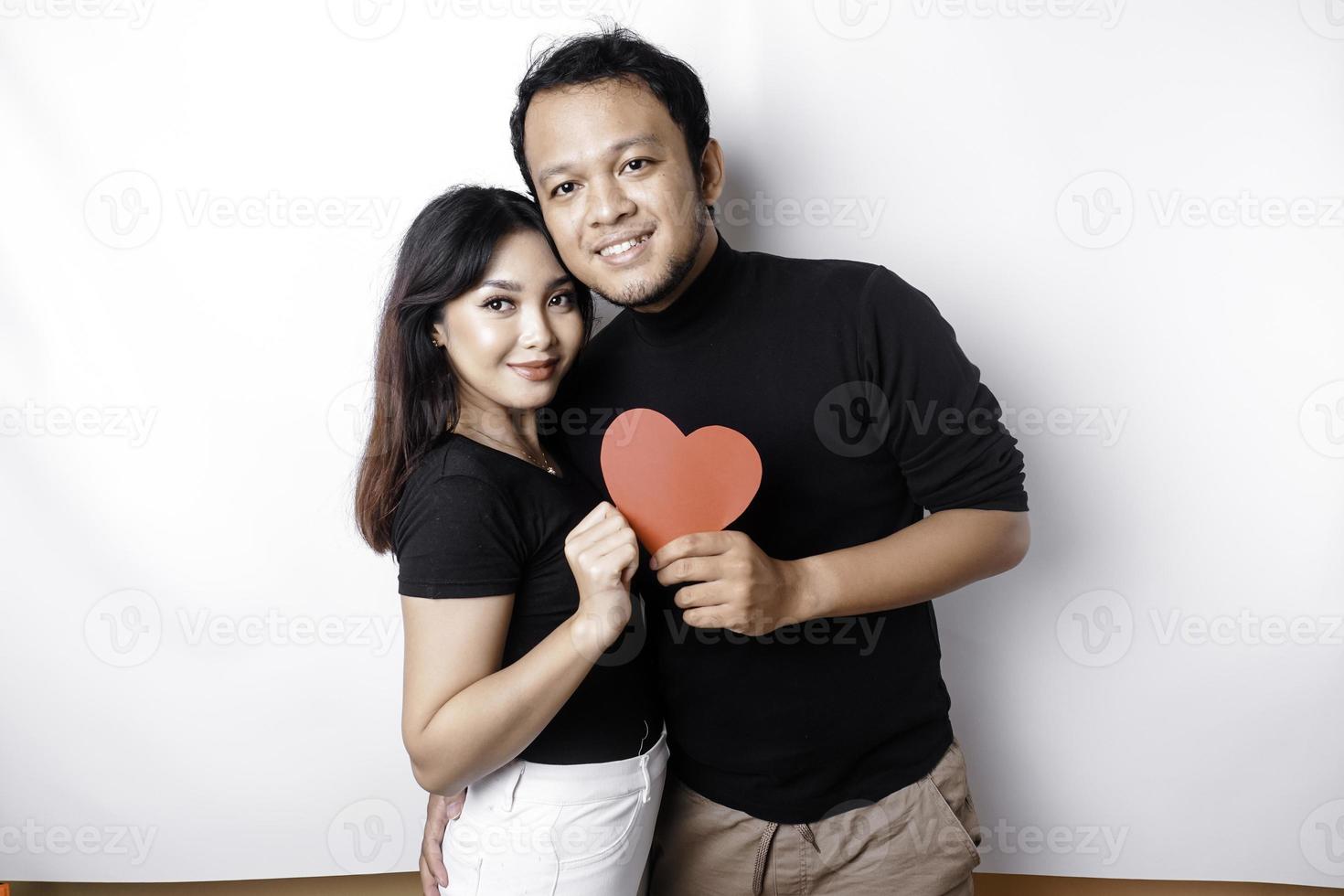 A young Asian couple smiling and holding red heart-shaped paper, isolated by white background photo