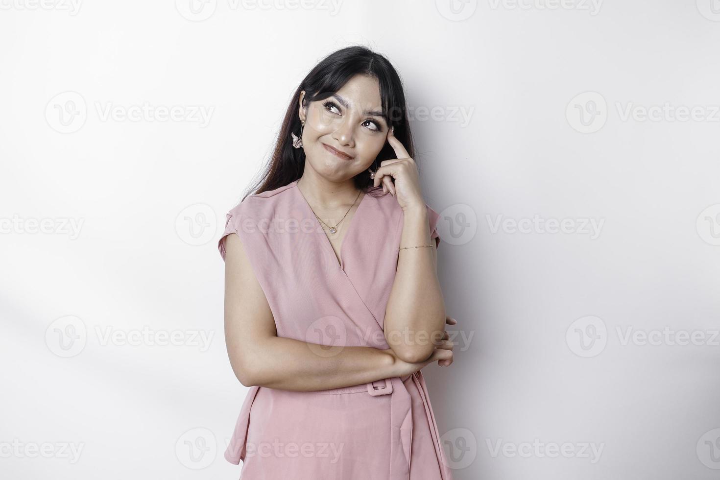 A thoughtful young woman dressed in pink blouse while looking aside, isolated by white background photo