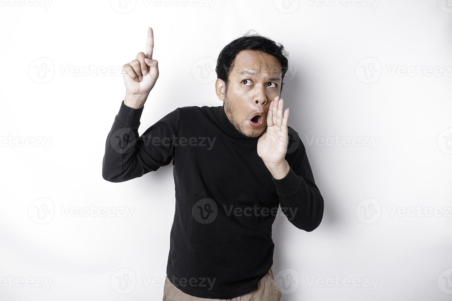 Shocked Asian man wearing black shirt pointing at the copy space on top of him, isolated by white background photo