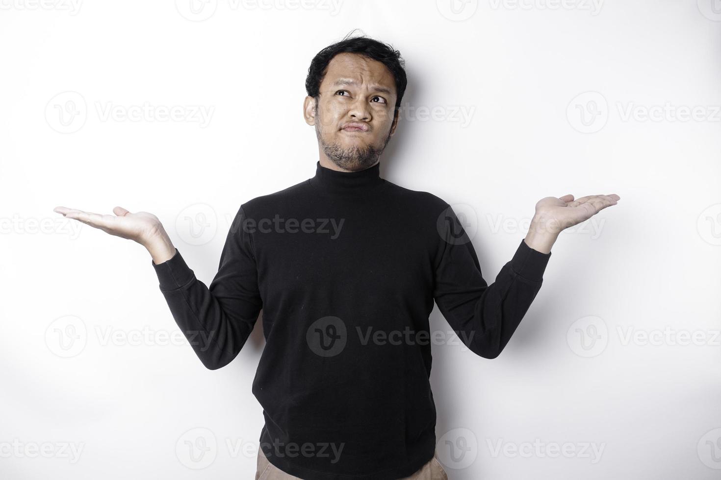 A portrait of an Asian man wearing a black shirt looks so confused between choices, isolated by a white background photo