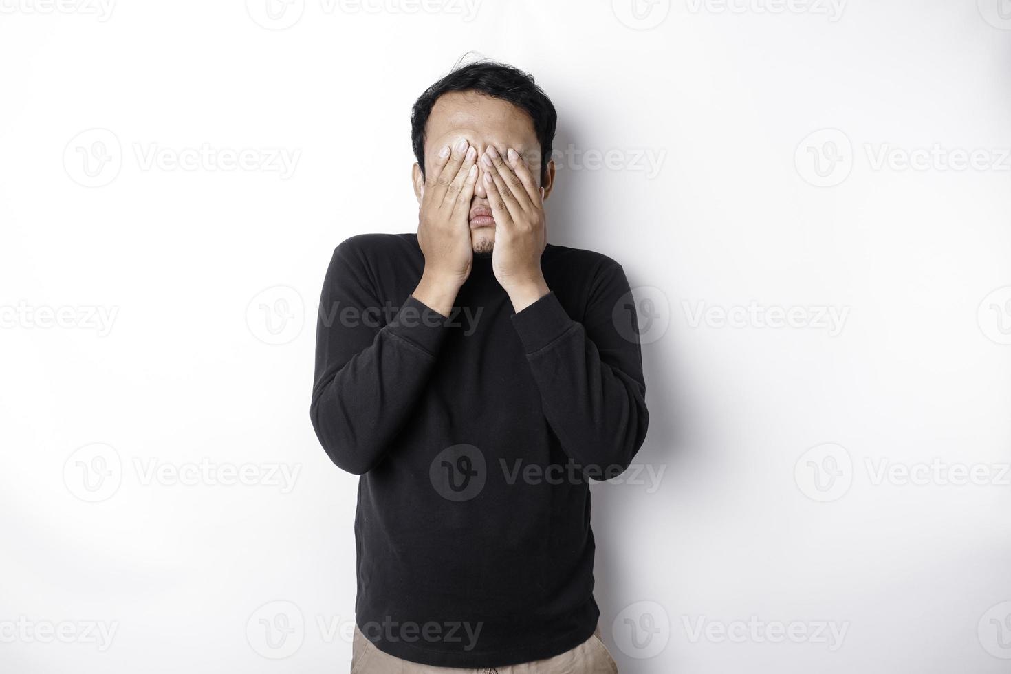 Portrait of sleepy attractive Asian man wearing a black shirt, feeling tired after night without sleep, yawning, covering opened mouth with palm photo