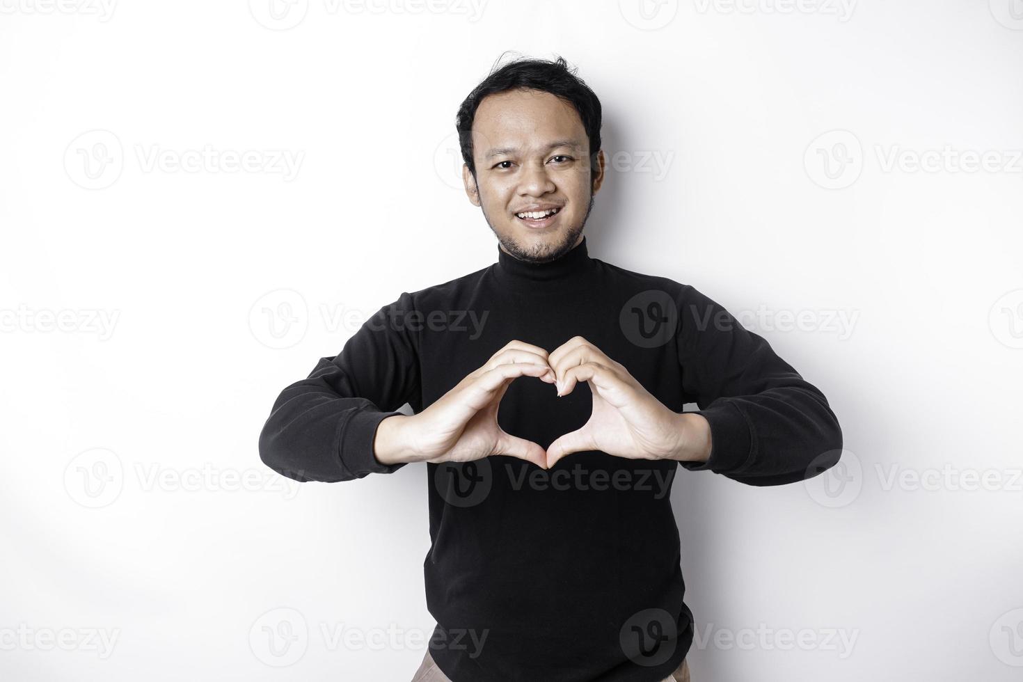 un contento joven asiático hombre vistiendo un negro camisa siente romántico formas corazón gesto expresando oferta sentimientos foto