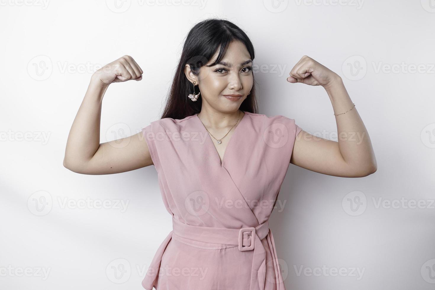emocionado asiático mujer vistiendo un rosado blusa demostración fuerte gesto por levantamiento su brazos y músculos sonriente con orgullo foto