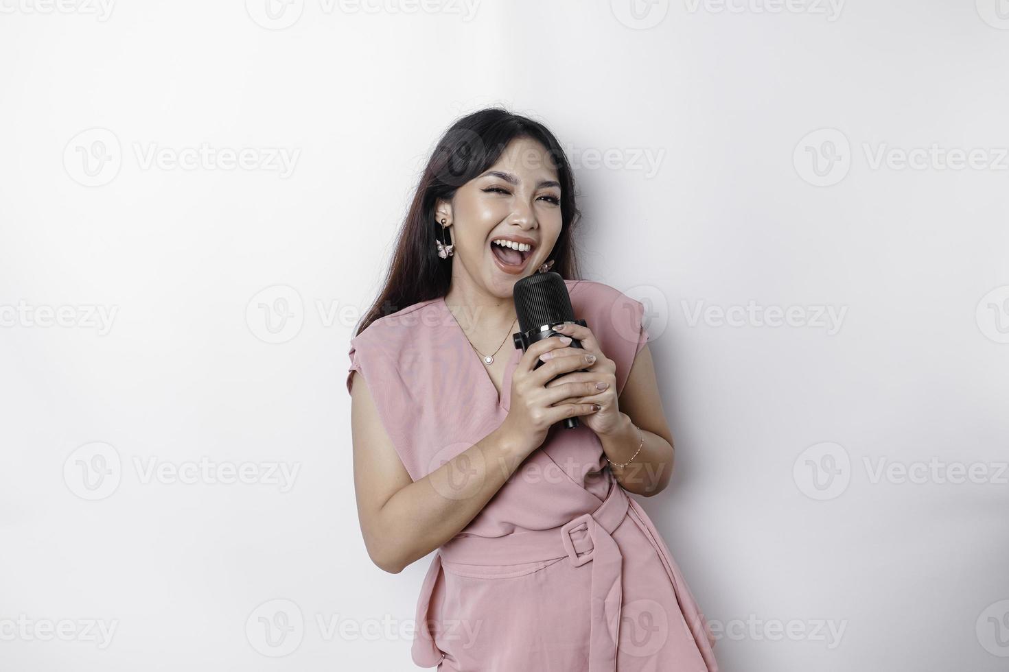 Portrait of carefree Asian woman, having fun karaoke, singing in microphone while standing over white background photo