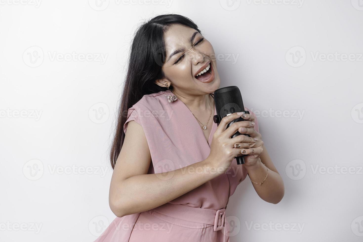 Portrait of carefree Asian woman, having fun karaoke, singing in microphone while standing over white background photo