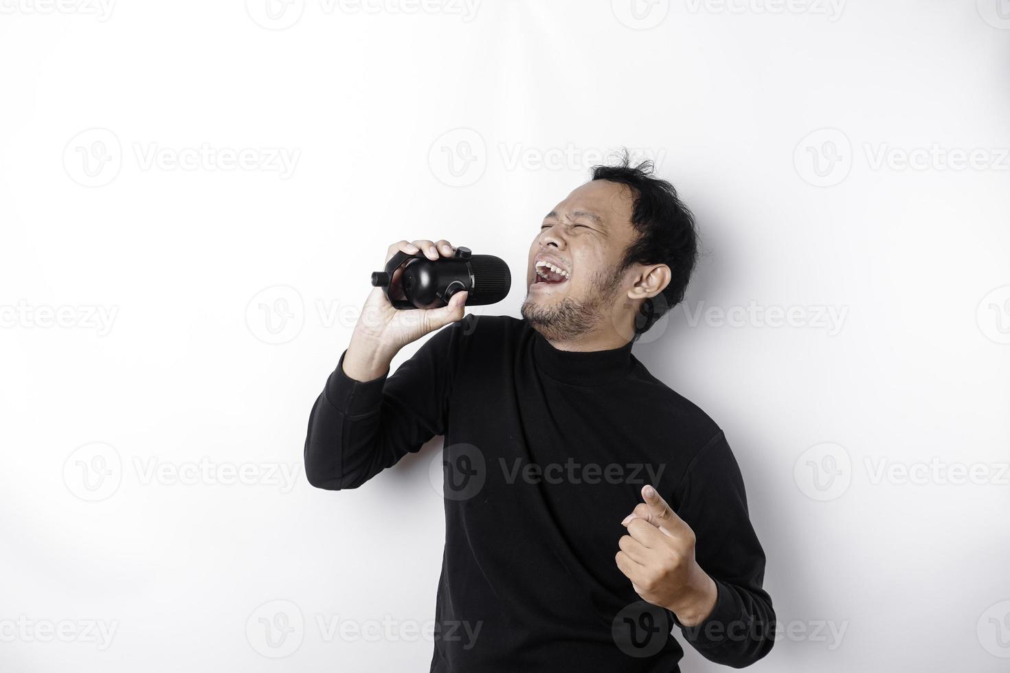Portrait of carefree Asian man, having fun karaoke, singing in microphone while standing over white background photo