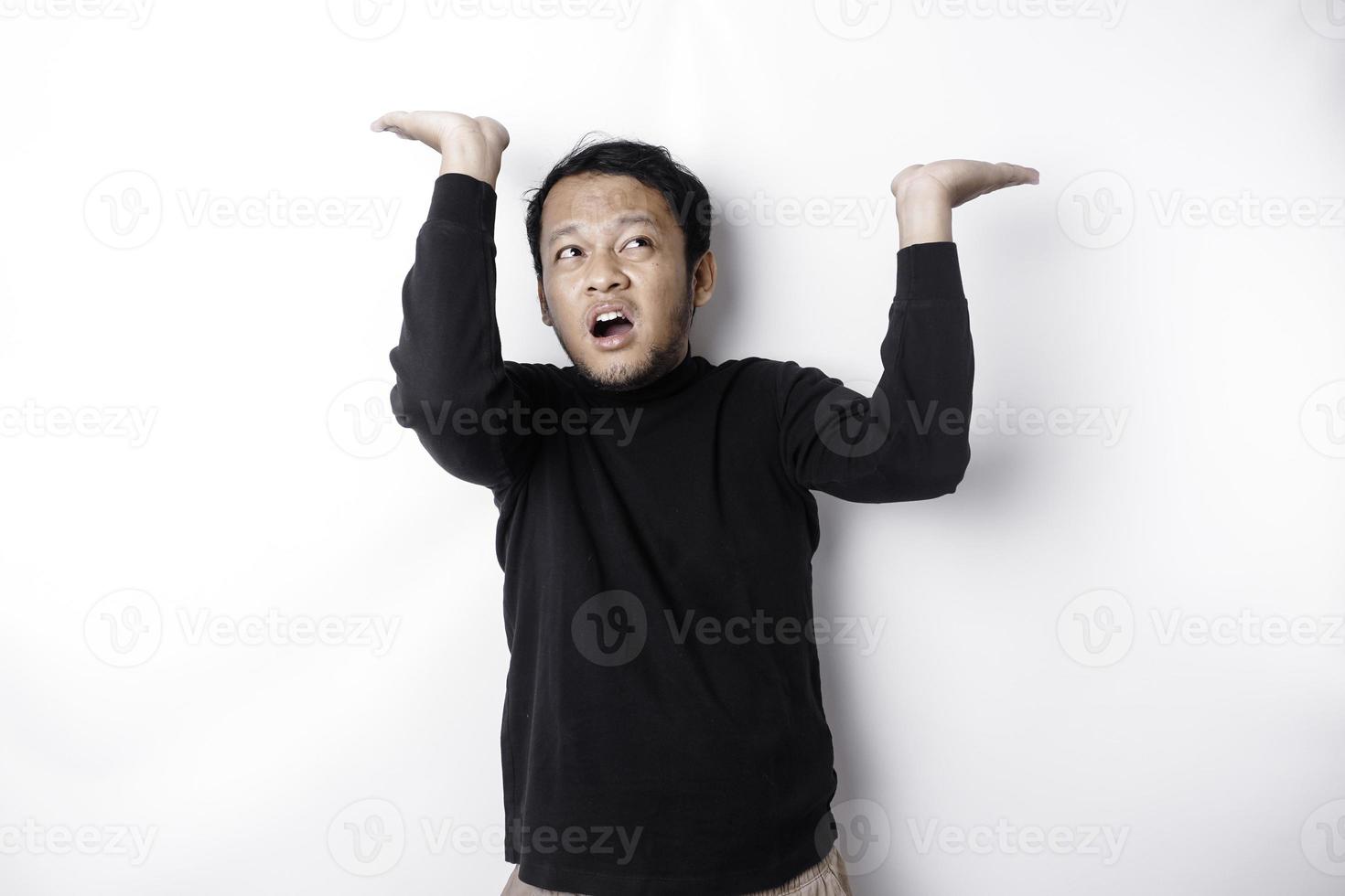 Shocked Asian man wearing black shirt pointing at the copy space on top of him, isolated by white background photo