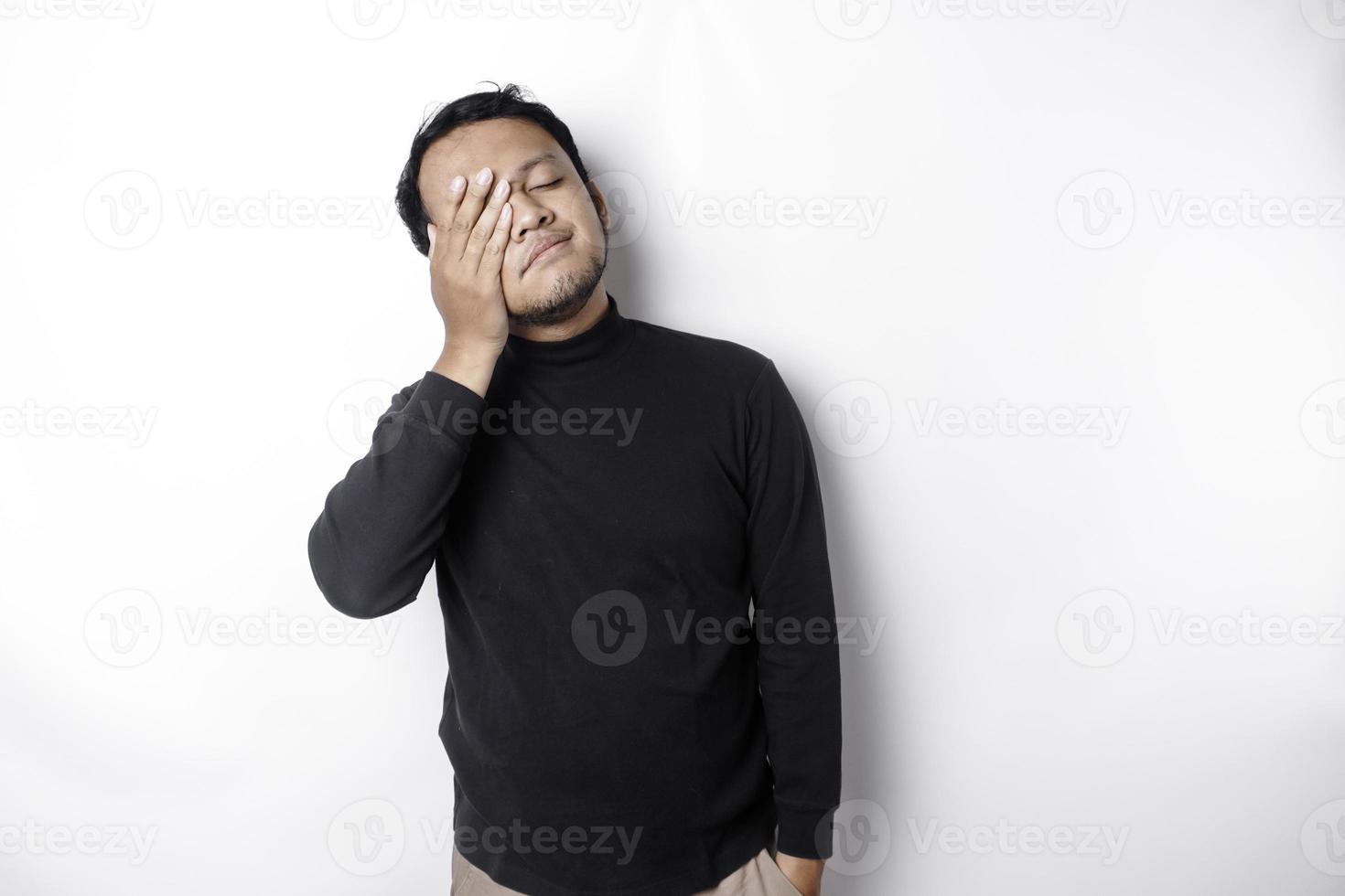 retrato de soñoliento atractivo asiático hombre vistiendo un negro camisa, sensación cansado después noche sin dormir, bostezando, cubierta abrió boca con palma foto