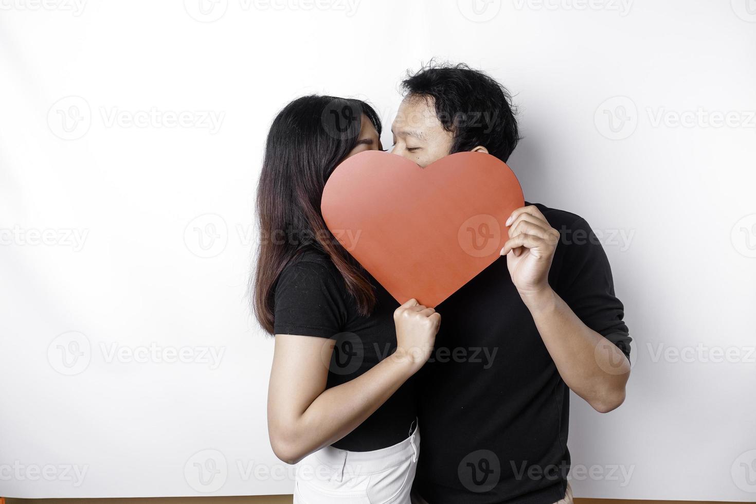 un Pareja en amor sostiene un papel rojo corazón, cubierta su caras. contento San Valentín día foto