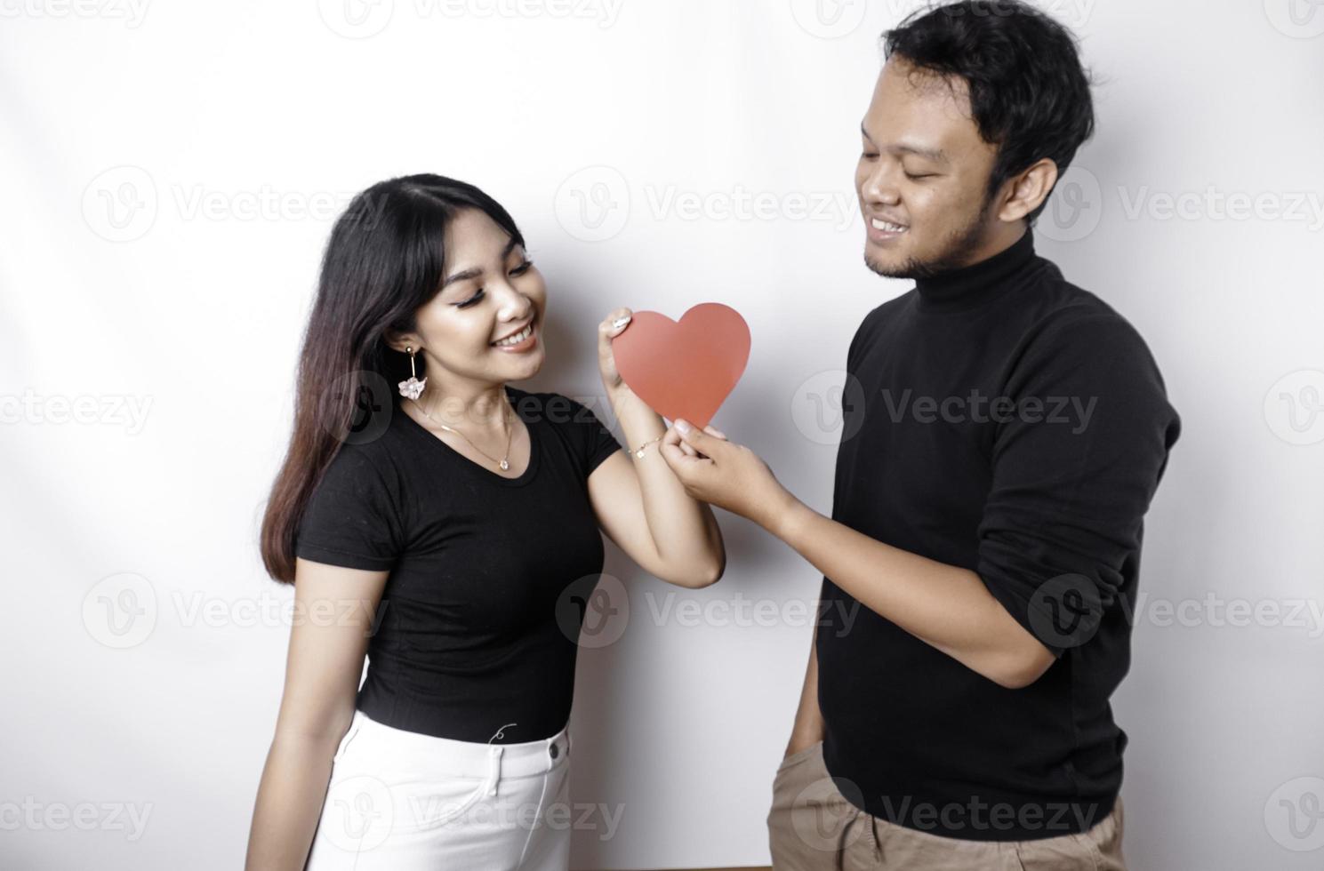 A young Asian couple smiling and holding red heart-shaped paper, isolated by white background photo